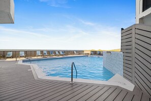 Un área de piscina con terraza de madera, sillas de descanso y un muro de azulejos.