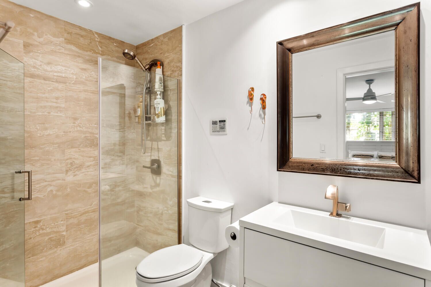 A modern bathroom with a glass-enclosed shower, a white toilet, and a large mirror with a wooden frame.