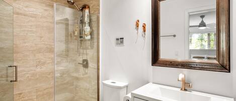A modern bathroom with a glass-enclosed shower, a white toilet, and a large mirror with a wooden frame.