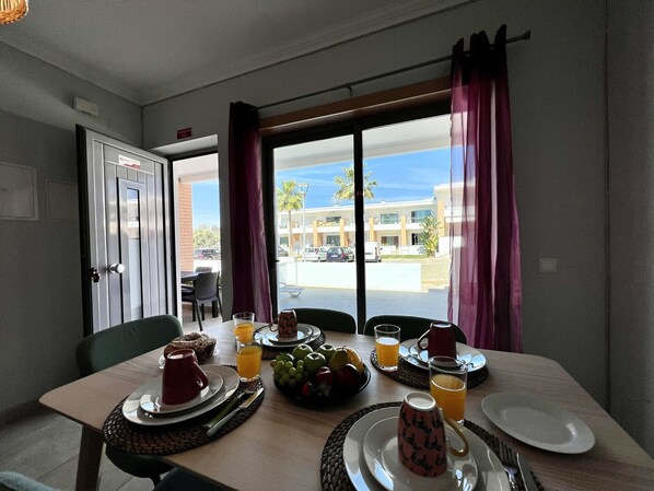 A breakfast table set with plates, cutlery, glasses of orange juice, and a bowl of fruit.