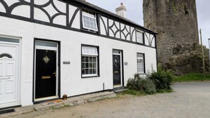 A white building with black trim and a black door, labeled "Y Bwllyn," next to a stone tower. - Y Bwthyn (Conwy)