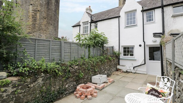 A courtyard with a stone wall, a brick fire pit, and a white metal table with a floral cushion. - Y Bwthyn (Conwy)