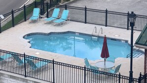 Una piscina con sillas azules y una mesa, rodeada por una valla negra.