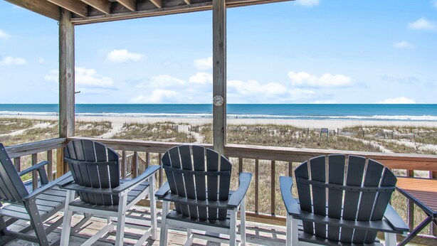 A wooden deck with three Adirondack chairs facing a beach view. - "All Good" Oceanfront 2 bedrooms, 2 bathrooms. (Holden Beach)