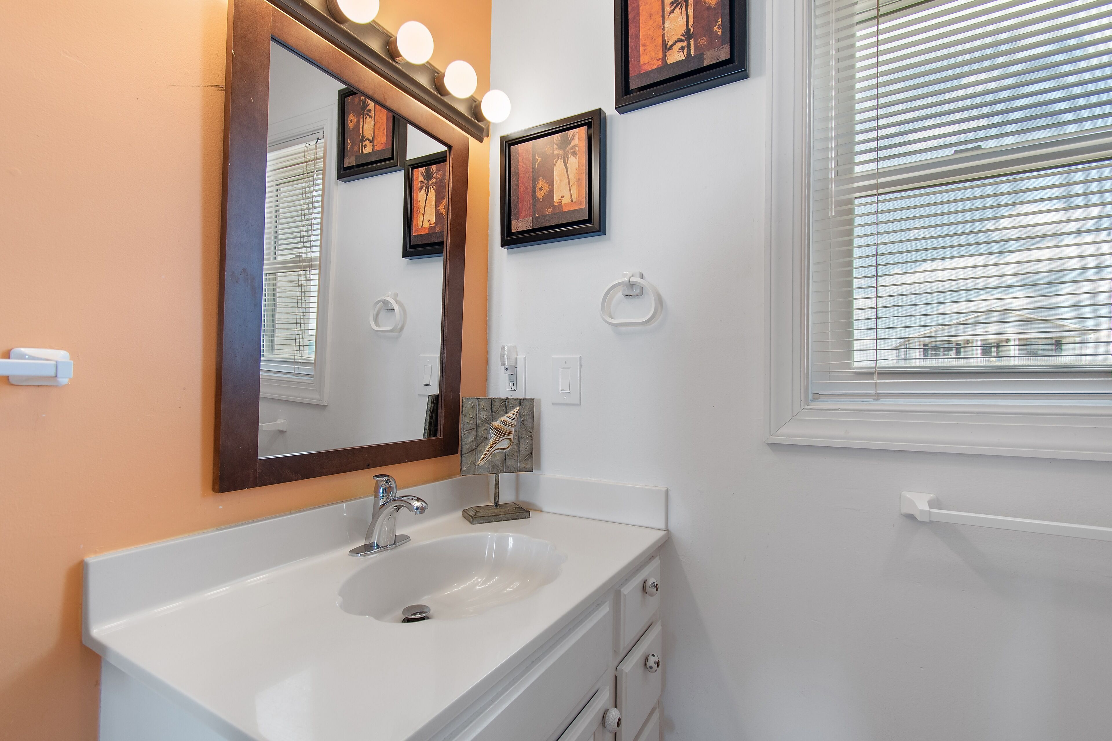 Une salle de bain avec un lavabo blanc, un miroir et des œuvres d’art encadrées accrochées au mur.