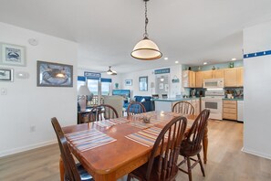 Uma sala de jantar espaçosa com uma mesa e cadeiras de madeira, um lustre e uma cozinha ao fundo.