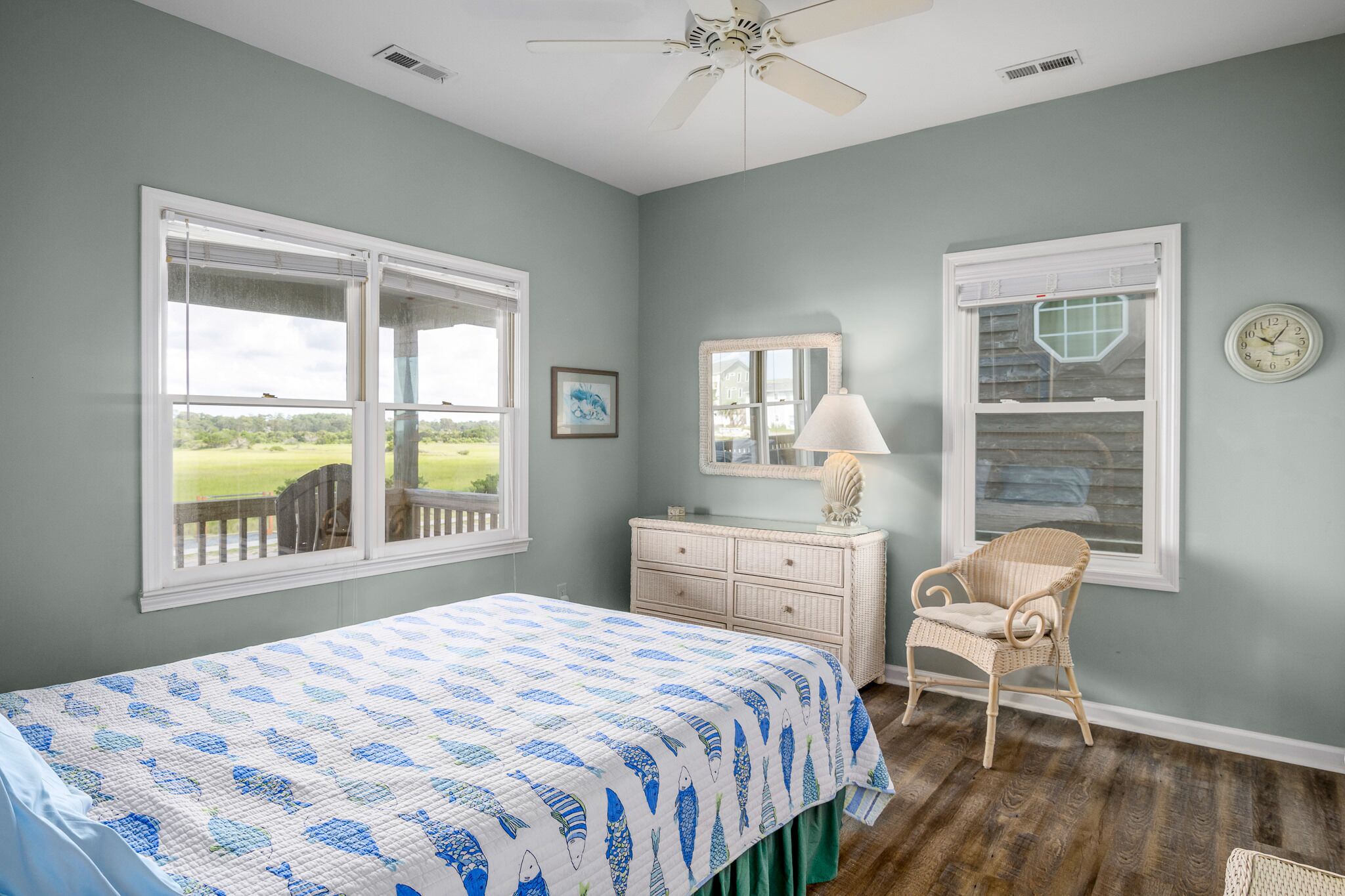 A bedroom with a bed, a chair, a dresser, a mirror, and two windows.