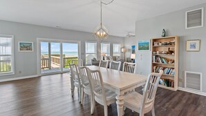 A spacious dining area with a large table and chairs, a chandelier, and a bookshelf.