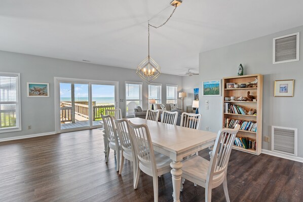 A spacious dining area with a large table and chairs, a chandelier, and a bookshelf.