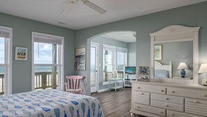 A bedroom with a bed, dresser, and a view of the ocean through large windows.