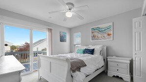 Ein Schlafzimmer mit einem Bett, einem Nachttisch, einem Deckenventilator und einem großen Fenster.