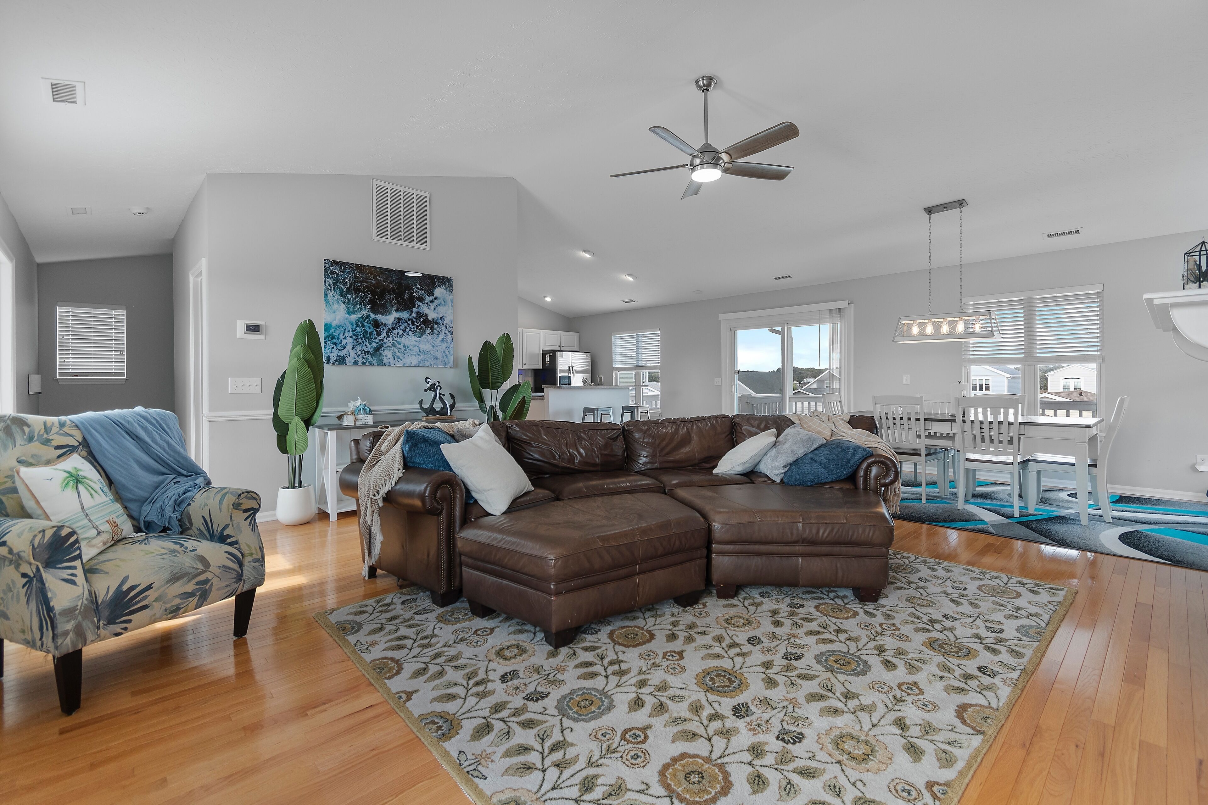 A spacious living room with a brown sectional sofa, a patterned rug, and a ceiling fan.