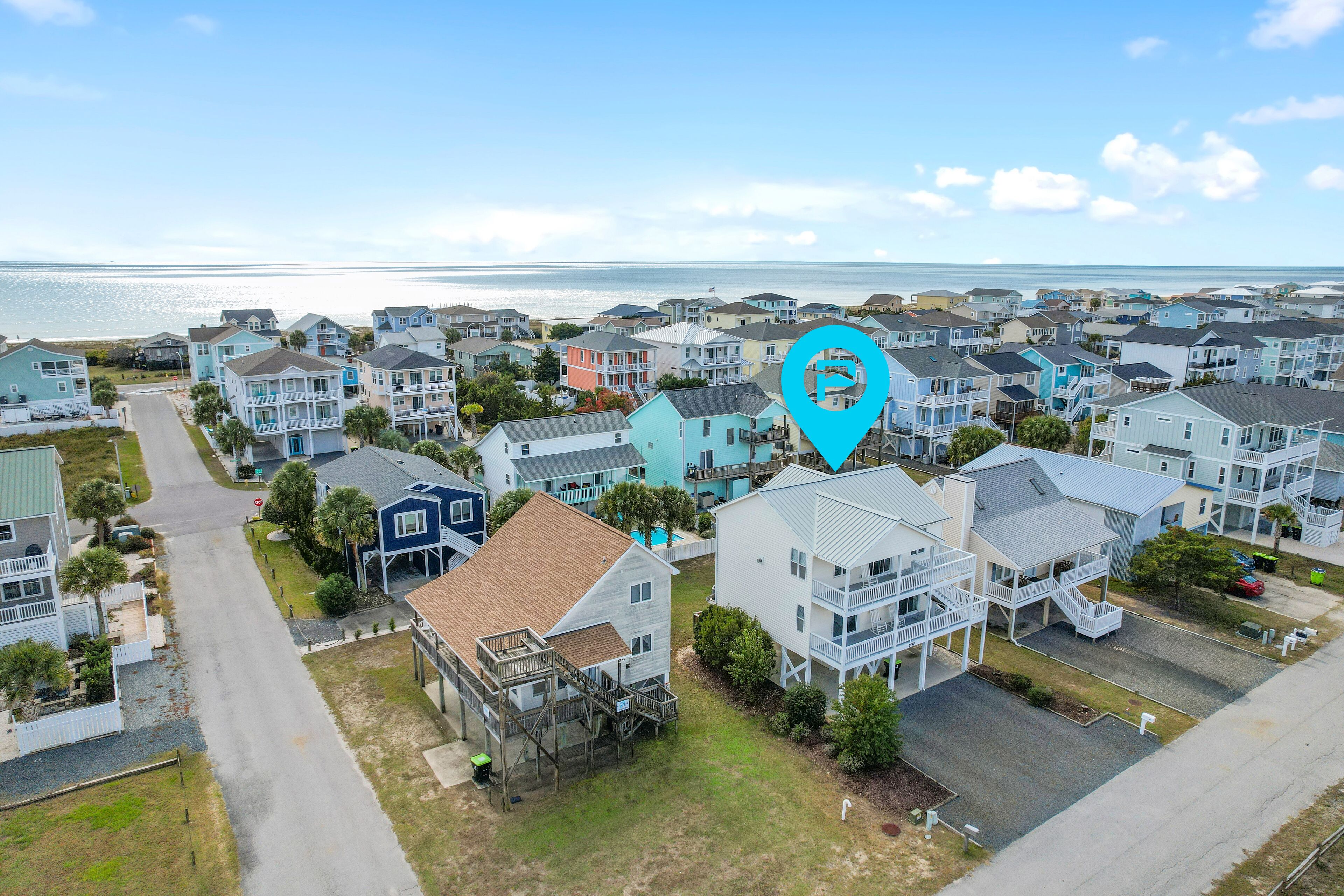 A coastal residential area with multiple two-story houses, a clear view of the ocean, and a road leading through the neighborhood.