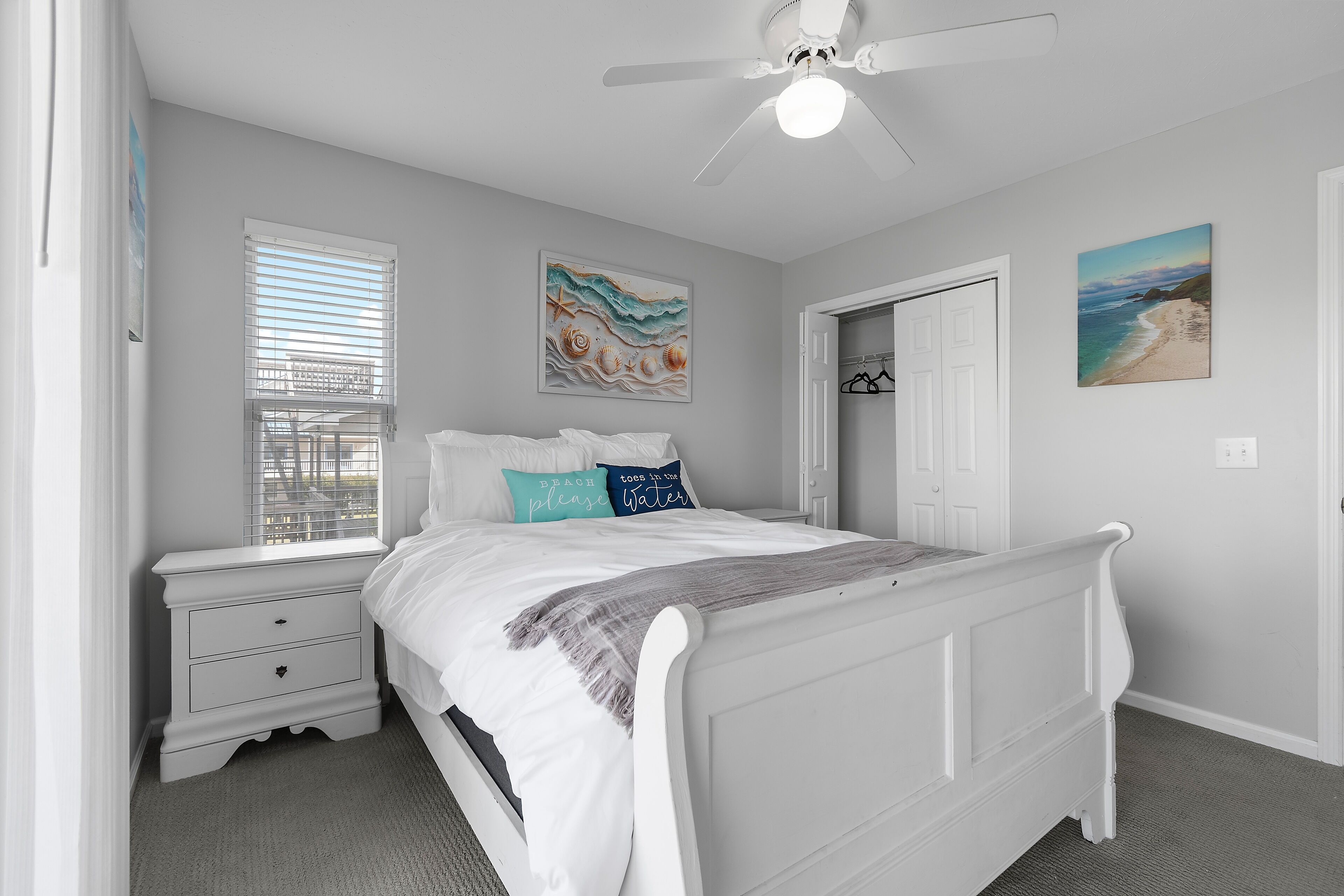 A bedroom with a white bed, a nightstand, a window with blinds, and a ceiling fan.