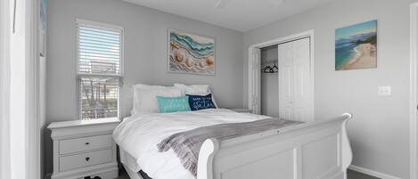 A bedroom with a white bed, a nightstand, a window with blinds, and a ceiling fan.