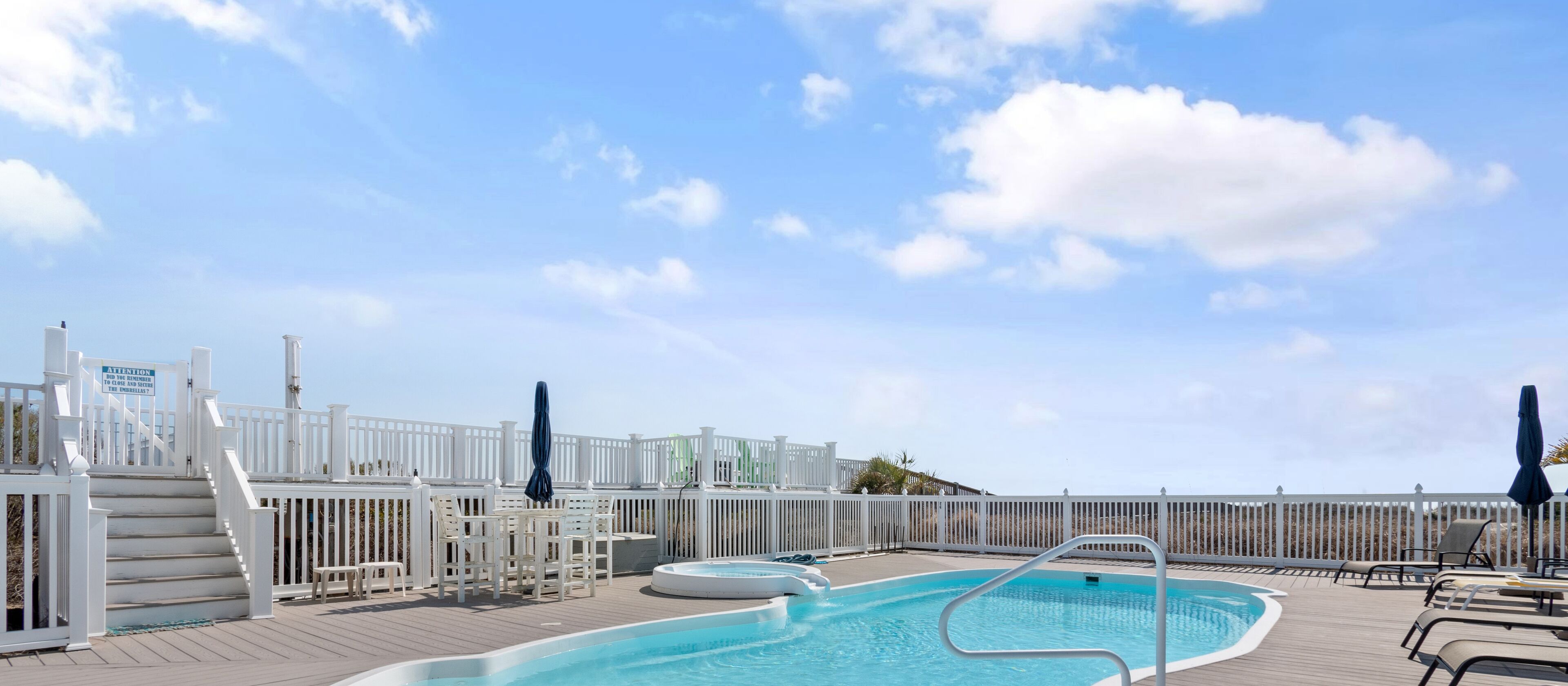 Un espace piscine doté d’une terrasse en bois, d’une clôture blanche et de chaises longues.