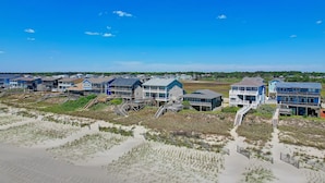 Une propriété située en bord de mer, comprenant plusieurs maisons reliées par des passerelles, avec des plages de sable fin et un ciel d’un bleu éclatant.