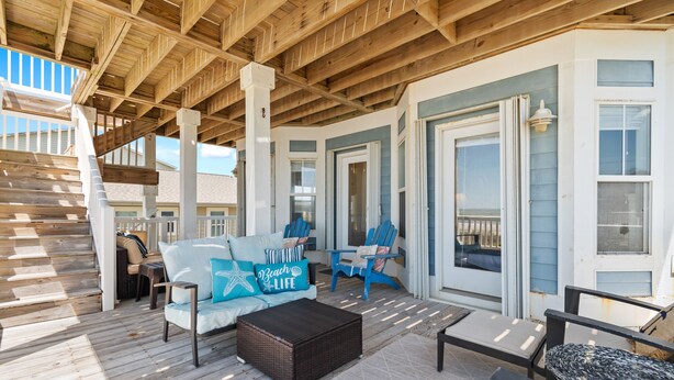 Un espace extérieur abrité, doté d’une terrasse en bois, d’un canapé agrémenté de coussins aux motifs marins et d’un pouf en osier.