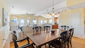 Un vaste espace dédié à la salle à manger, avec une grande table en bois et de nombreuses chaises, un ventilateur de plafond et un lustre.