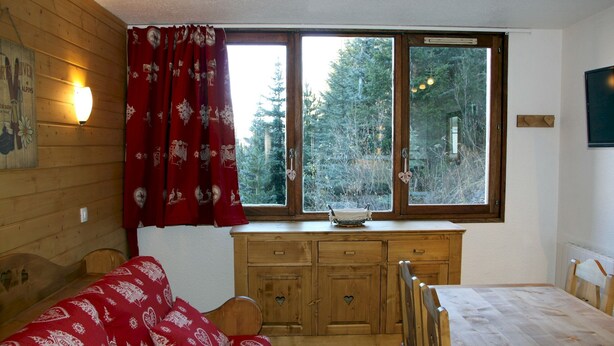 Ein gemütliches Blockhauszimmer mit einem hölzernen Bett, einem Holztisch, einem Fenster mit Blick auf Bäume, einem Holzschrank und einer Wandleuchte.