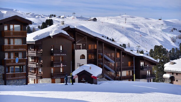 A snow-covered lodge with multiple balconies and a ski slope in the background.