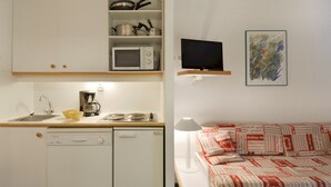 A compact kitchen with a dishwasher, microwave, and coffee maker. There is a small TV and a painting on the wall.