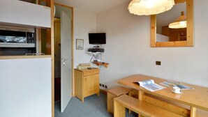 Una habitación pequeña con una mesa de madera, un banco y un televisor sobre un mueble.