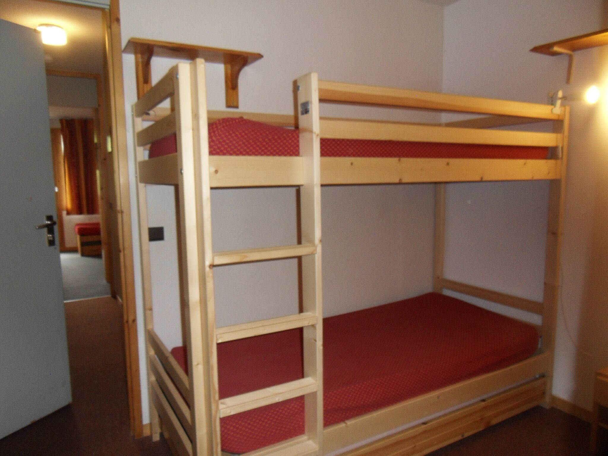Un lit superposé avec une échelle, un matelas rouge et une structure en bois.