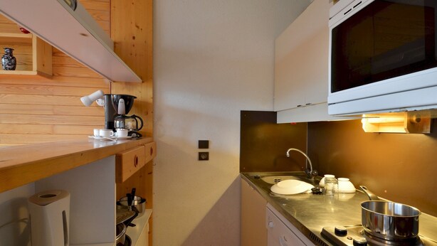 Cocina compacta con microondas, estufa, lavamanos y estantes de madera.