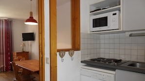 Cocina compacta con estufa, microondas y lavavajillas. Hay una mesa de comedor con sillas y una lámpara colgante roja.