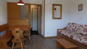Una habitación acogedora con una mesa de madera, sillas, un banco, un sofá con estampado y un espejo en la pared, además de una lámpara colgante.