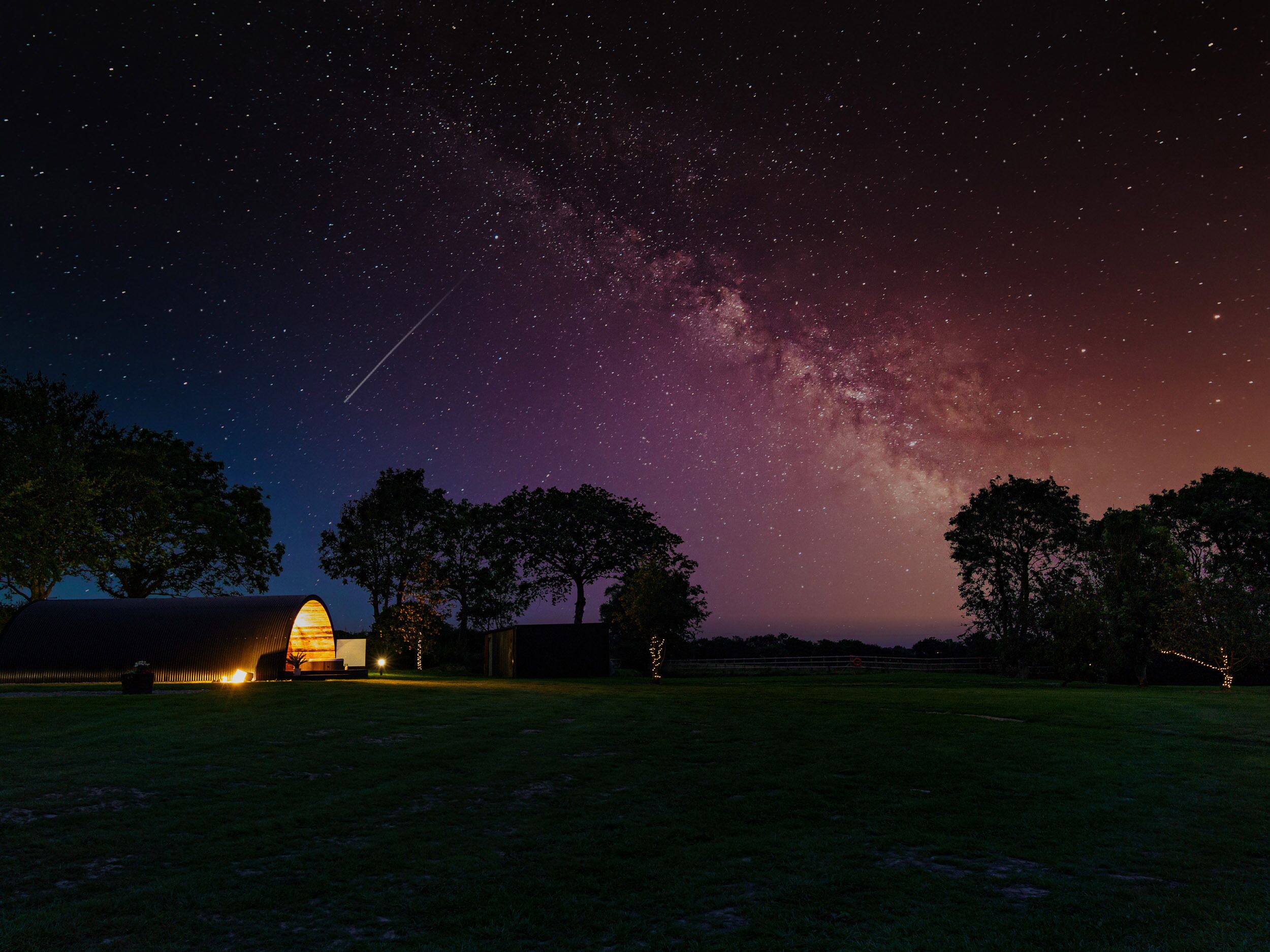 Cielo estrellado con la Vía Láctea visible, un granero y árboles en un campo.