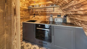A compact kitchen with wooden walls, a sink, a stove, and a toaster.