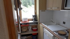 A compact kitchen with a sink, stove, and microwave. There is a window with a view of trees. - travelski home classic - Résidence 3000 - Studio 4 personnes 529 (La Plagne)