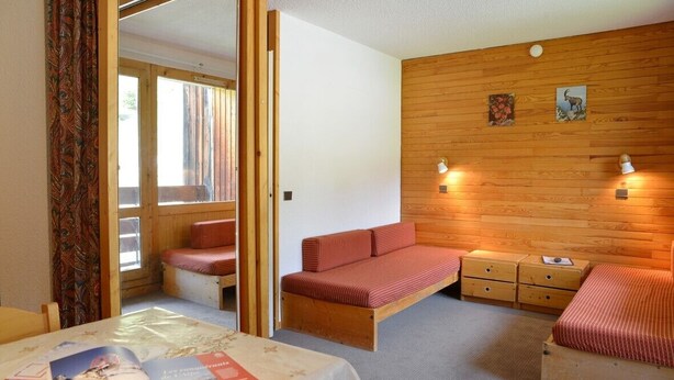 A compact room with a bed, a small table with a magazine, and a bench. - travelski home classic - Résidence 3000 - Studio 4 personnes 529 (La Plagne)