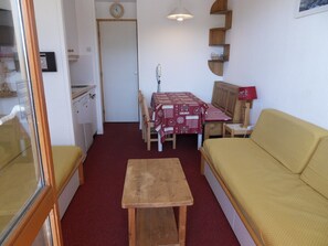 A compact living space with a kitchenette, a dining table with chairs, a sofa, and a small table.