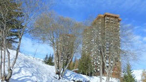 A multi-story building with a modern architectural design, surrounded by trees and covered in snow. - travelski home classic - Résidence Phénix - 2 Pièces 5 personnes Vue Vallée 0305 (Villarembert)