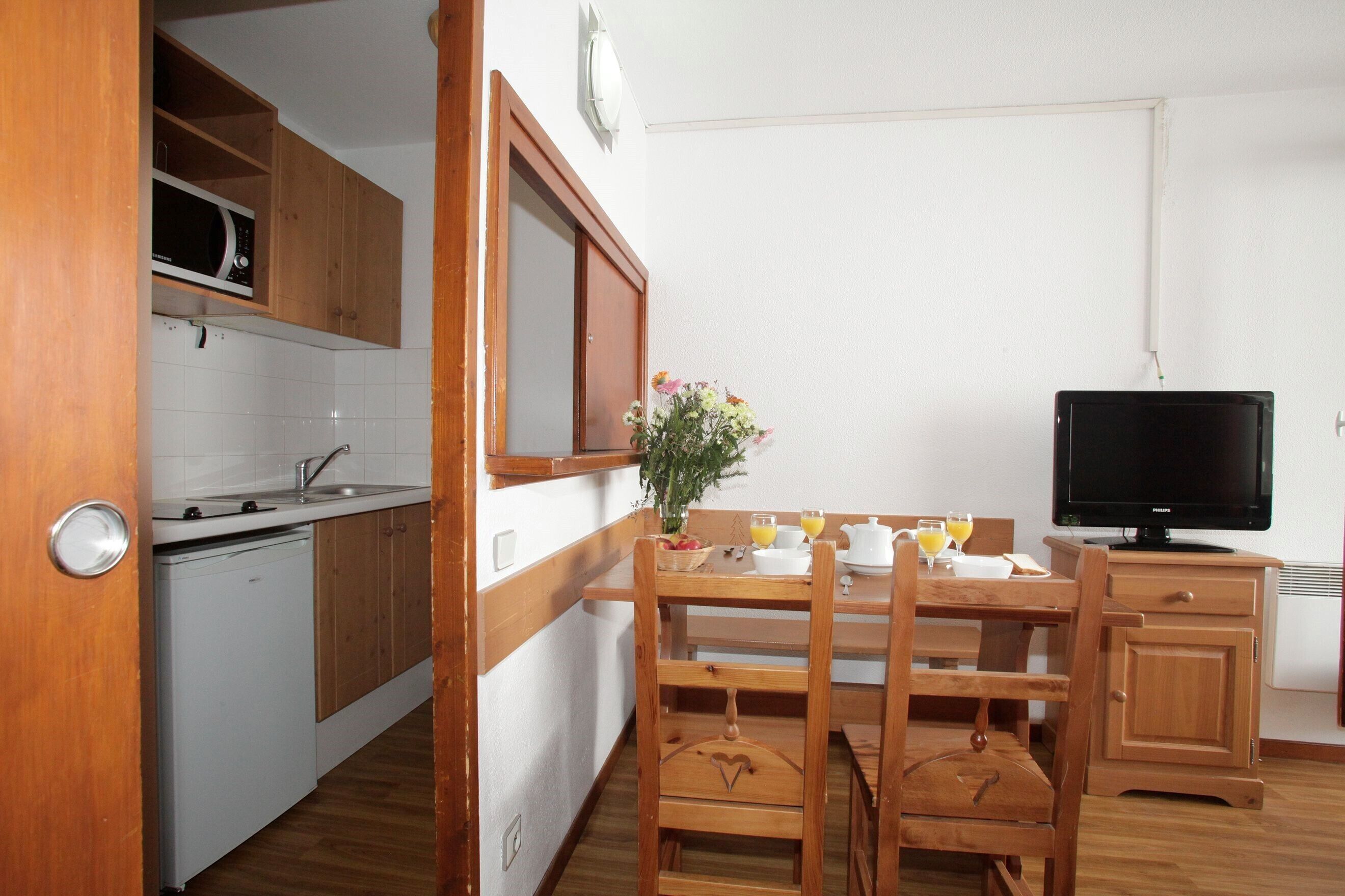 A compact kitchen with wooden cabinets, a microwave, a sink, and a dining area with a table and chairs.