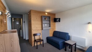 Ein kompakter Wohnraum mit blauem Sofa, einem kleinen Tisch, einem Holzschrank und einem an der Wand montierten Fernseher.