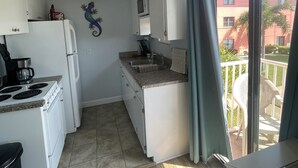 Eine kompakte Küche mit weißen Geräten, einer kleinen Arbeitsfläche und Blick auf den Balkon.