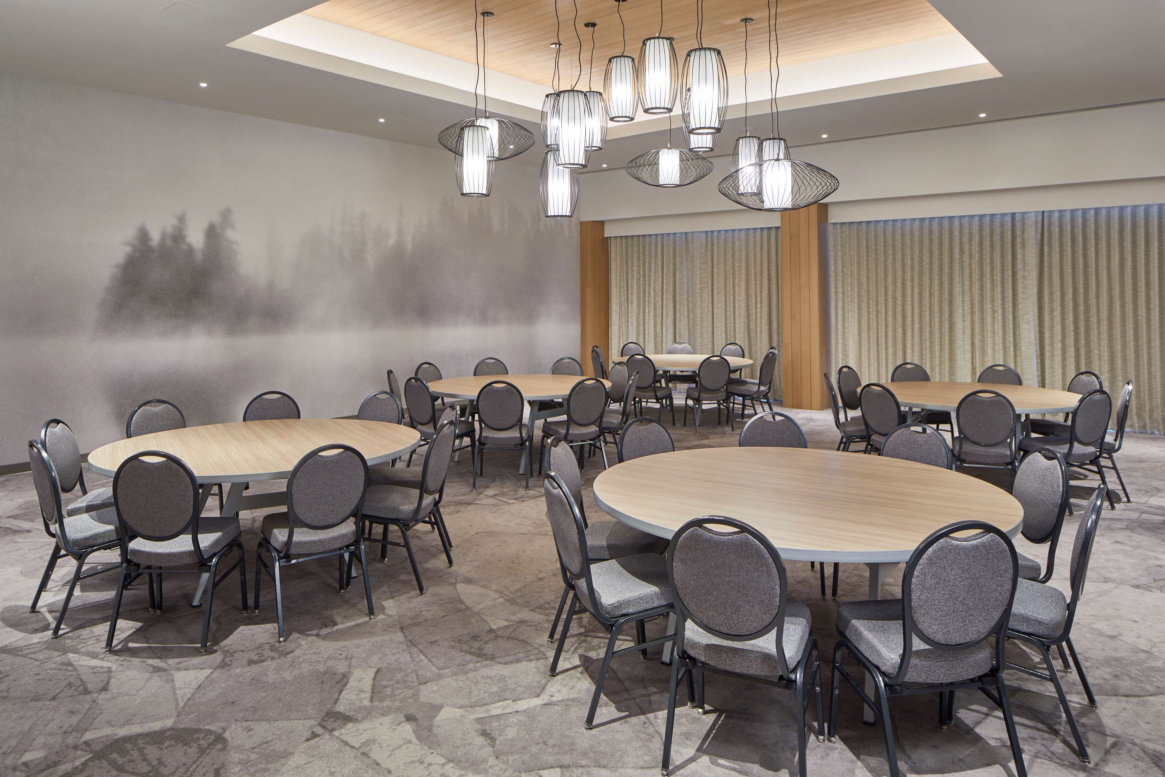 Un salón de conferencias con mesas y sillas redondas, una lámpara de araña grande y un mural de un bosque brumoso en la pared.