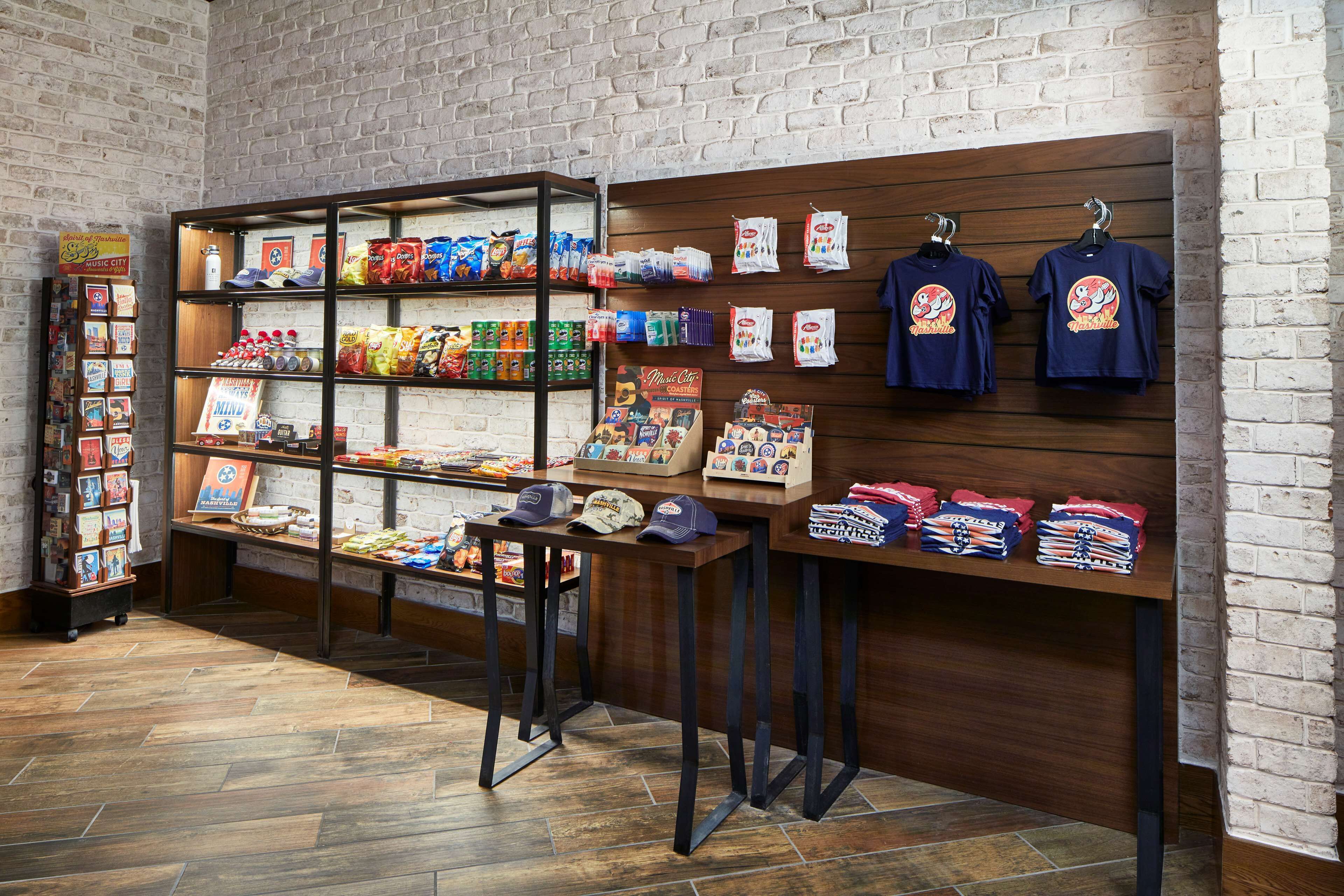 A retail space with shelves stocked with snacks, a display of hats, and T-shirts on racks.