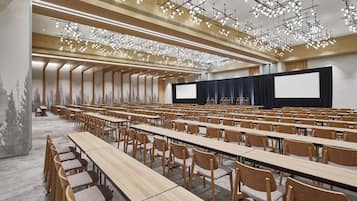 A conference room with rows of tables and chairs, a large screen, and a ceiling with hanging lights.