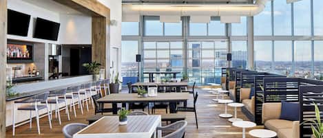 A modern bar area with seating and large windows offering a city view.