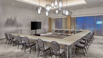 A conference room with a long table, multiple chairs, a TV, and a city view through large windows.