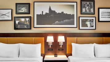 Habitación de hotel con dos camas, una obra de arte con paisaje urbano, fotografías enmarcadas y una mesita de noche con dos lámparas.