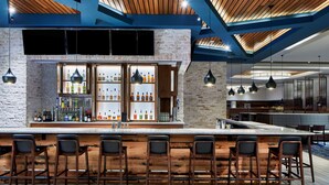 A bar area with wooden bar stools, a brick wall, and a ceiling with exposed beams. - Embassy Suites by Hilton Nashville Downtown (Nashville)