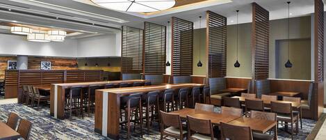 A hotel lobby with a modern design, featuring wooden paneling, a patterned carpet, and a variety of seating arrangements including tables and booths.