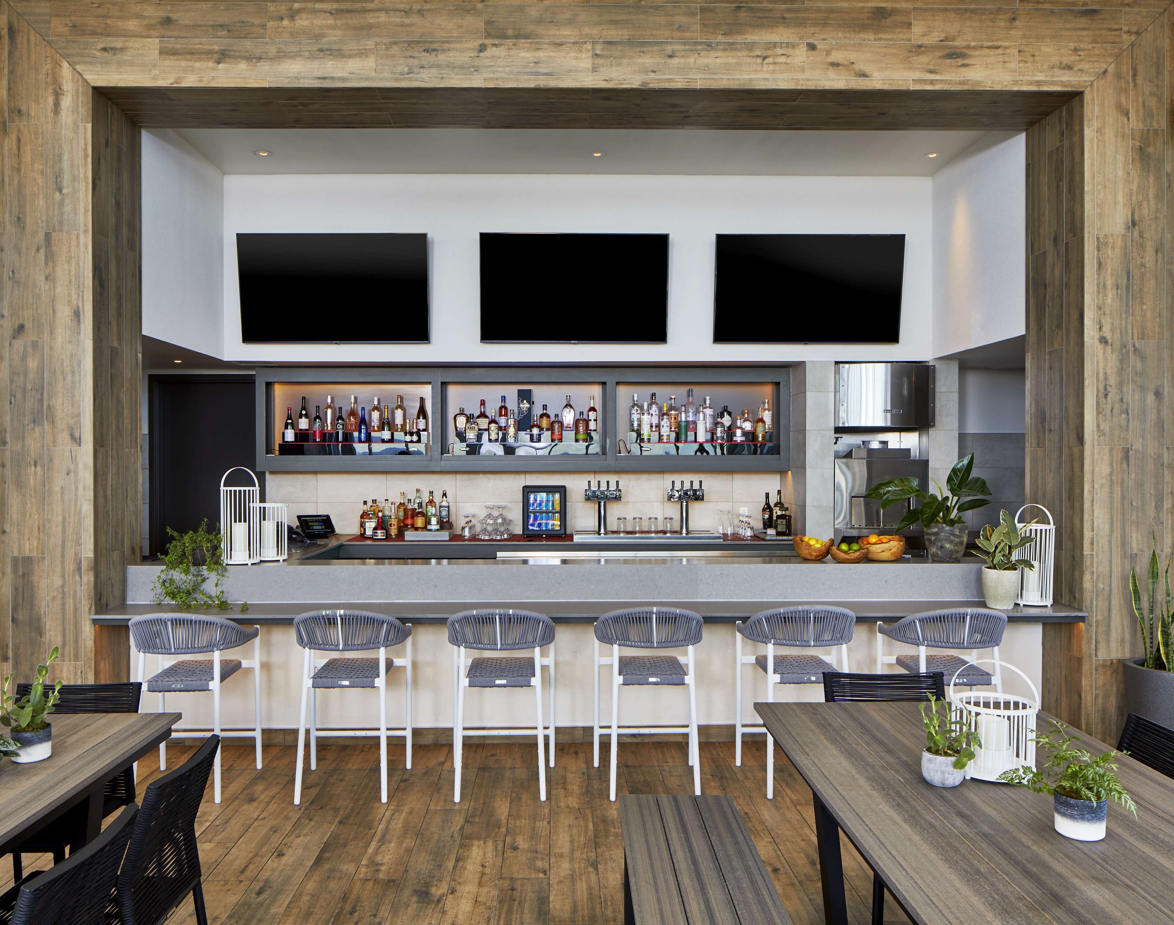A modern bar area with a long counter, multiple seating options, and a variety of bottles and glasses.