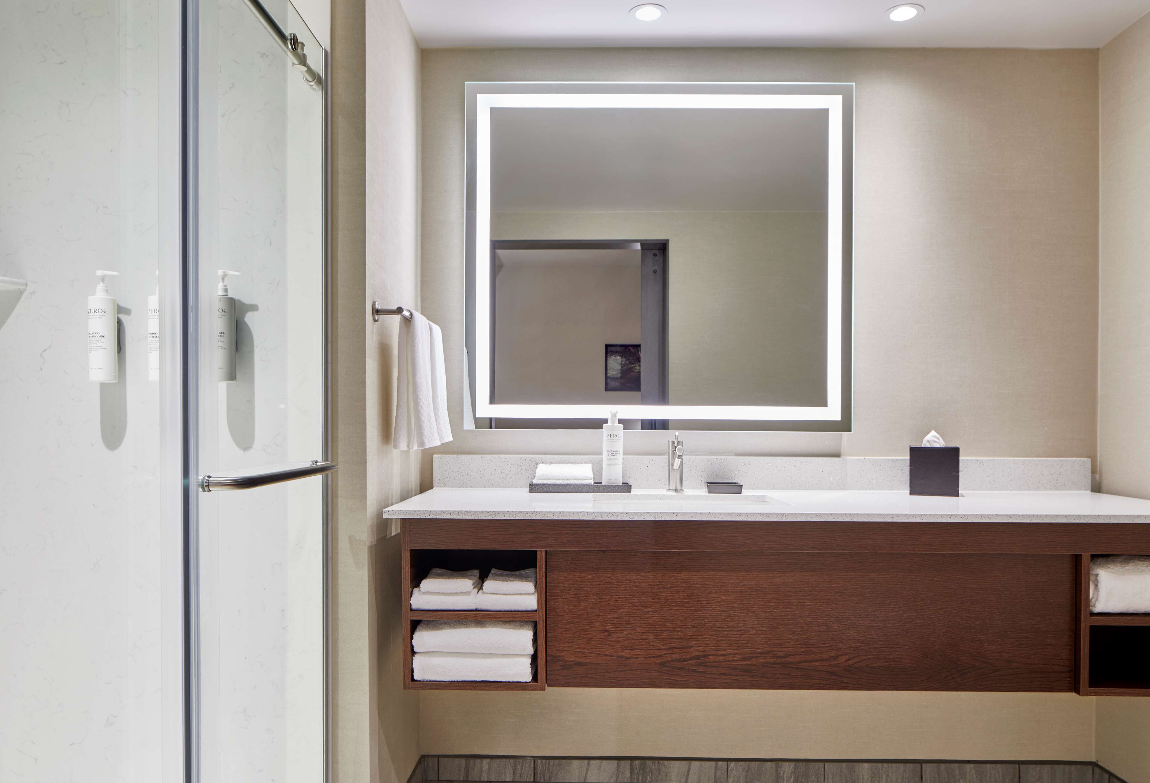 A modern bathroom with a glass shower enclosure, a large mirror, a wooden vanity, and built-in towel racks.